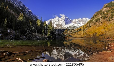 Panorama image of Maroon Bells peaks in the Elk Mountains reflecting on Maroon Lake in early morning sunlight