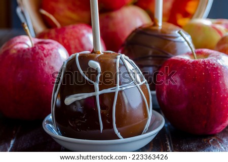 Close up of gourmet caramel apples with nuts and chocolate drizzle with red apples spilling out of bushel basket