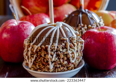 Close up of hand dipped caramel apples with nuts and chocolate drizzle with red apples spilling out of bushel basket