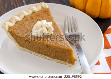 Single slice of homemade pumpkin pie with dollop of whipped cream sitting on white plate with fork and orange chevron napkin