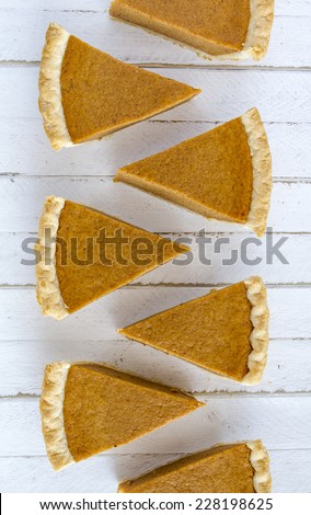 7 slices of homemade pumpkin pie in row sitting on white wooden table