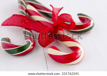 3 large red, white and green striped candy canes tied with red burlap ribbon sitting on white wooden table