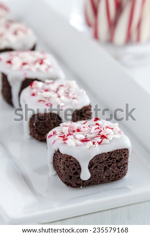 Fresh baked chocolate brownie bites covered with white icing and candy cane sprinkles sitting on white plate