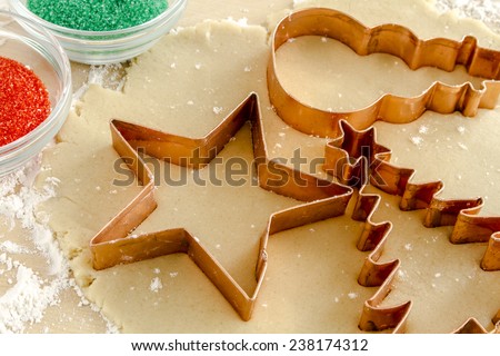 Star, snowman and Christmas tree copper cookie cutters cutting out holiday sugar cookies with red and green sugar sprinkles