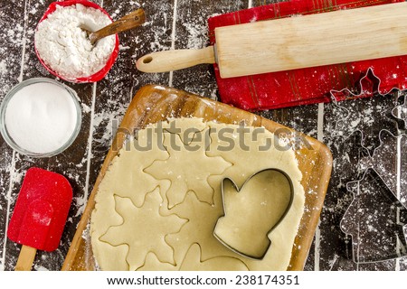 Snowflake and mitten cookie cutters cutting out holiday sugar cookies with wooden rolling pin and red spatula and colorful kitchen towel