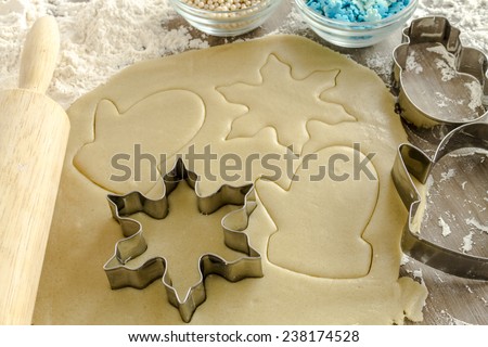 Snowflake, snowman and mitten cookie cutters cutting out holiday sugar cookies with wooden rolling pin and white dragees and blue snowflake candy sprinkles