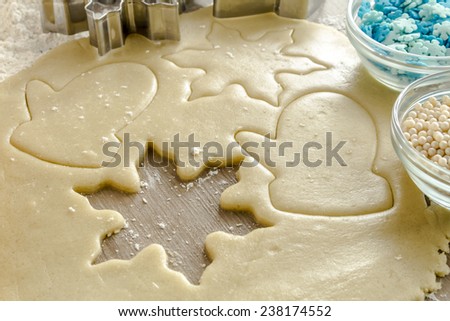 Snowflake and mitten cookie cutters cutting out holiday sugar cookies with wooden rolling pin and white dragees and blue snowflake candy sprinkles