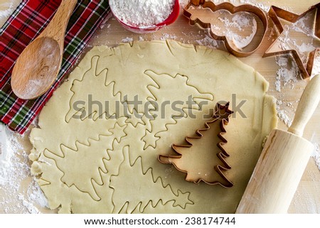 Copper cookie cutters cutting out holiday sugar cookies with wooden rolling pin and spoon and colorful kitchen towel