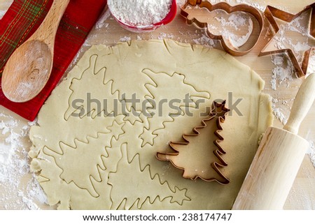 Copper cookie cutters cutting out holiday sugar cookies with wooden rolling pin and spoon and colorful kitchen towel