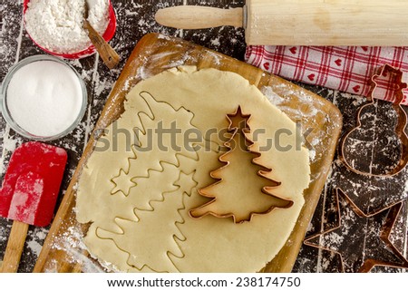 Copper cookie cutters cutting out holiday sugar cookies with wooden rolling pin and red spatula sitting on dark wood table