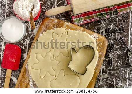 Snowflake and mitten cookie cutters cutting out holiday sugar cookies with wooden rolling pin and red spatula and colorful kitchen towel