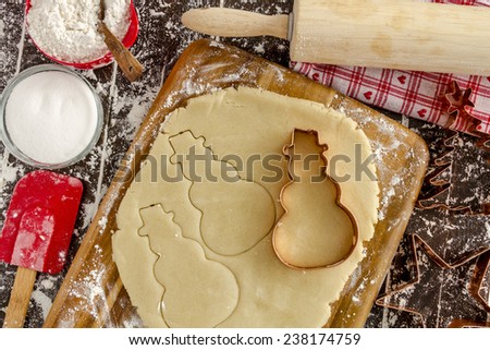 Copper cookie cutters cutting out holiday sugar cookies with wooden rolling pin and red spatula sitting on dark wood table
