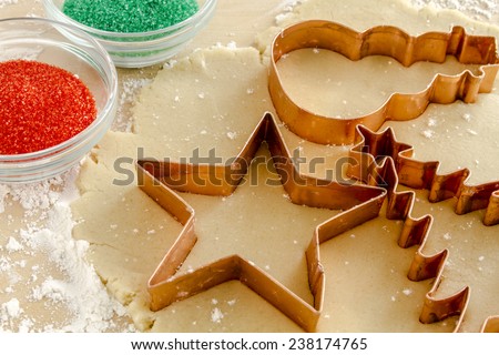 Star, snowman and Christmas tree copper cookie cutters cutting out holiday sugar cookies with red and green sugar sprinkles