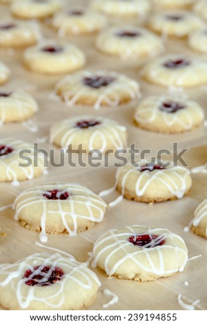 Rows of raspberry thumbprint cookies with powdered sugar frosting drizzle sitting on wax paper