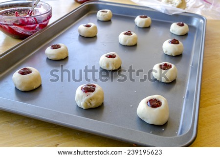 Rows of raspberry thumbprint cookies sitting on baking sheet waiting to go into oven