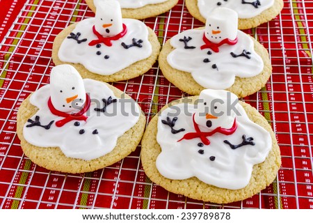 Melting snowman sugar cookies sitting on wire baking rack with colorful holiday napkin