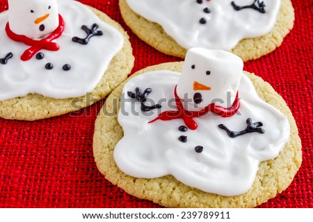 Close up of melting snowman sugar cookies sitting on red burlap fabric