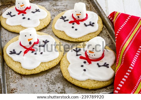 Melting snowman sugar cookies sitting on metal baking sheet with colorful holiday napkin