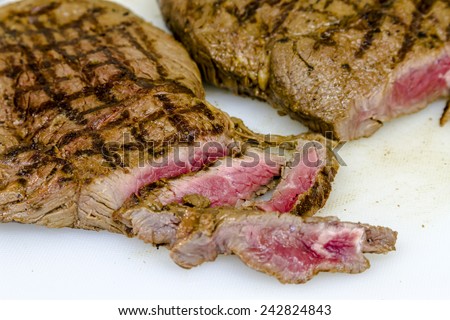 Rare top sirloin steaks with grill marks and several cut slices sitting on white cutting board