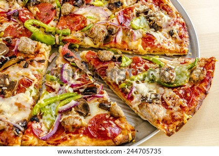 Close up of sliced thin crust supreme pizza sitting on metal pizza pan with fresh meats and vegetables