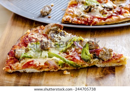Slice of thin crust supreme pizza sitting on wooden cutting board