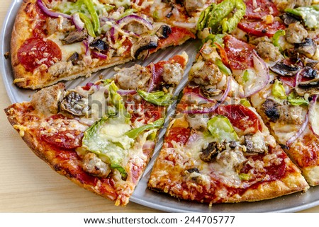Sliced thin crust supreme pizza sitting on metal pan made with fresh sausage, pepperoni, mushrooms, onions, green pepper and melted cheese