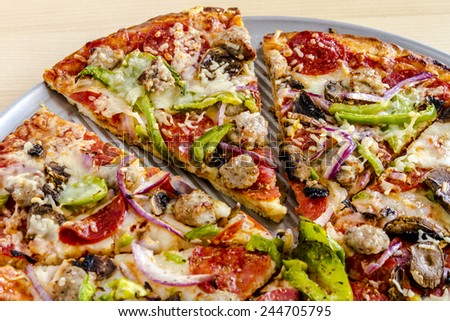 Close up of sliced thin crust supreme pizza sitting on metal pizza pan with fresh meats and vegetables