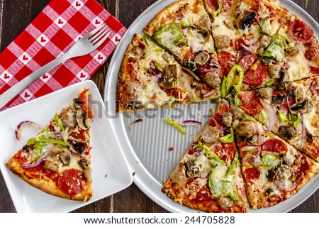 Fresh baked slice of thin crust supreme pizza sitting on white square plate with red heart napkin and fork
