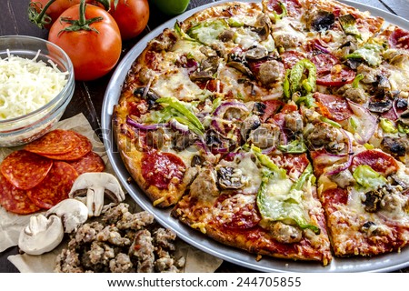 Close up of fresh baked thin crust supreme pizza surrounded by sausage, pepperoni, mushrooms, cheese and tomato ingredients