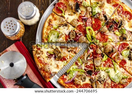 Sliced fresh baked thin crust supreme pizza sitting on metal pan with shakers of red pepper flakes and parmesan cheese with striped napkin and pizza cutter