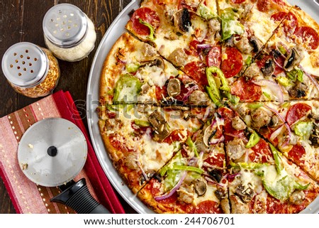 Sliced fresh baked thin crust supreme pizza with fresh mushrooms, onions, green peppers, tomato sauce, pepperoni, sausage and cheese with striped napkin and pizza cutter
