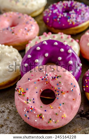 Row of homemade vanilla bean donuts with colorful icing sitting a metal baking pan