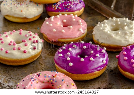 Close up of assortment of homemade vanilla bean donuts with colorful icing sitting on metal baking pan
