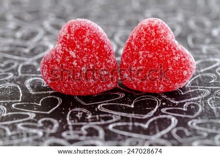 Two cinnamon heart candies coated with sugar sitting on black chalk board heart background