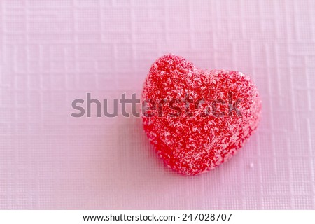 Single cinnamon heart candy coated with sugar sitting on pink textured background