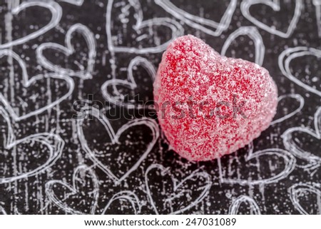 Single cinnamon heart candy coated with sugar sitting on black chalk board heart background
