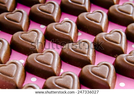 Rows of chocolate heart shaped candies filled with fudge sitting on pink polka dot background