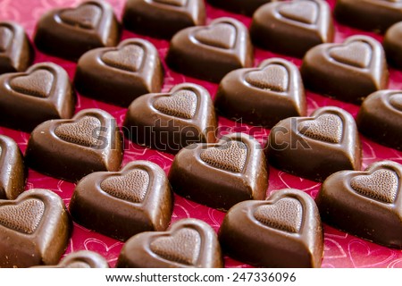 Rows of chocolate heart shaped candies filled with fudge sitting on red heart background