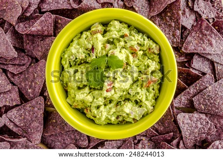 Homemade chunky guacamole in bright green bowl surrounded by blue corn tortilla chips