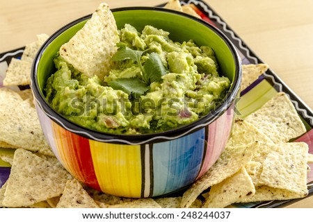 Homemade chunky guacamole in colorful bowl garnished with white corn tortilla chip and cilantro