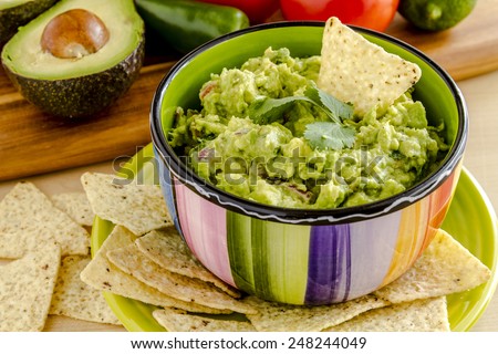 Fresh chunky guacamole in colorful bowl garnished with white corn tortilla chip and cilantro