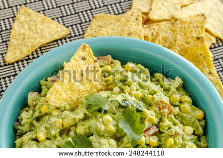Close up of homemade chunky guacamole with fresh corn in bright blue bowl and yellow corn tortilla chips