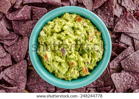 Homemade chunky guacamole in bright blue bowl surrounded by blue corn tortilla chips