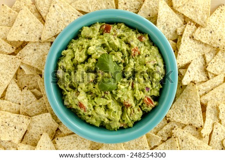 Homemade chunky guacamole in bright blue bowl surrounded by white corn tortilla chips