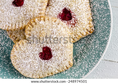 Close up of heart shaped cherry hand pies sitting on blue plate dusted with powdered sugar