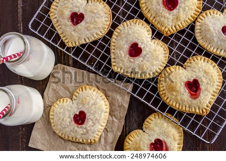 Heart shaped cherry hand pies sitting on wire cooling rack with two bottles of milk with red and white straws