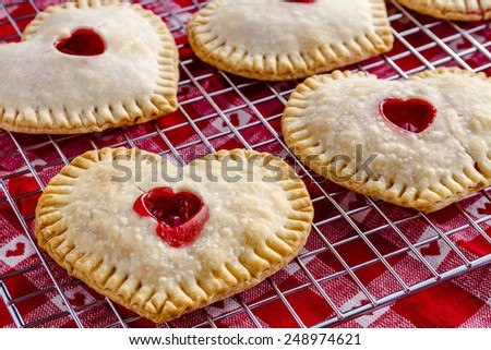 Heart shaped cherry hand pies sitting on wire cooling rack on top of red and white heart kitchen towel