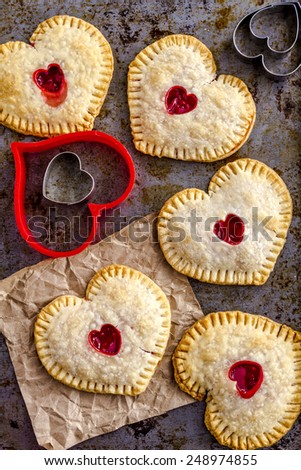 Heart shaped cherry hand pies sitting on metal baking pan with heart cookie cutters