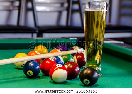 Colorful billiard balls and pool stick sitting on pool table with glass of beer