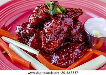 Spicy BBQ buffalo chicken wings sitting on plate garnished with carrot and celery sticks with blue cheese dipping sauce